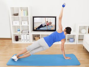 Young Woman Exercising On Mat In Front Of Television